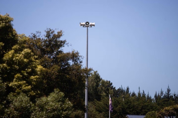 a tsunami siren sticks up above a tree line at a domain